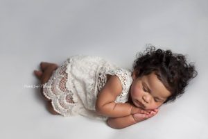 A 1 year old sleeps in side lying pose on the beanbag wearing a vintage dress. 