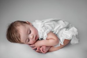 A 1 year old girl sleeping in taco pose on the beanbag, wearing a vintage dress. 
